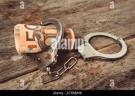 Roll euro money bills on a wooden table in handcuffs. Handcuffs and money on table. Financial crime, dirty money and corruption concept. Euro bills wi Stock Photo