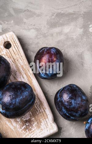 Fresh ripe plum fruits with water drops on wooden cutting board, stone concrete background, top view Stock Photo