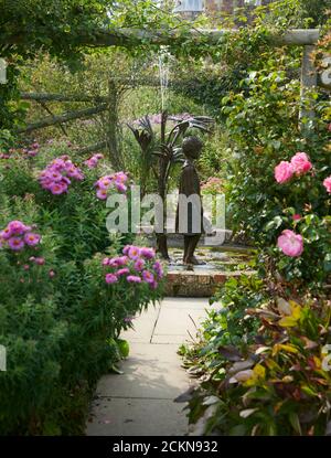 Looking down the Herbaceous borders of a walled garden towards a water feature in the form of a little girl. England, UK, GB. Stock Photo