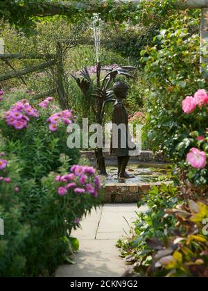 Looking down the Herbaceous borders of a walled garden towards a water feature in the form of a little girl. England, UK, GB. Stock Photo