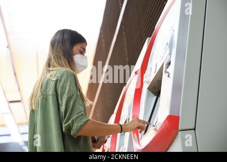 Young woman wearing face mask, buying a ticket at the train machines. Public transport concept. Stock Photo