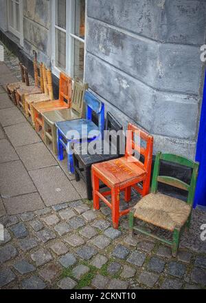 A still life of multi colored childrens wooden chairs all in a row on a street. Stock Photo