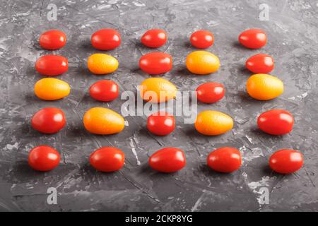 Rows of cherry tomatoes and kumquats on a black concrete background, side view, contrast concept. Stock Photo