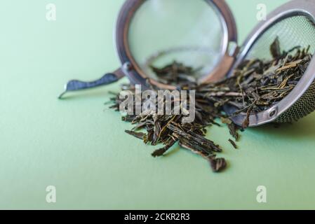 close up view of light green table surface with an open tea filter and dry leaves of green tea on the top Stock Photo