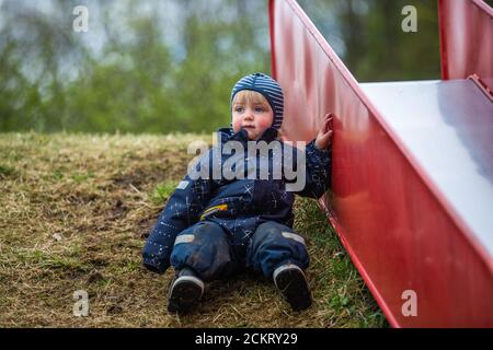 Young boy wearing a puddle suit leaning on a slide Stock Photo