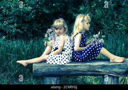 two beautiful blond girls sitting on bench in meadow Stock Photo