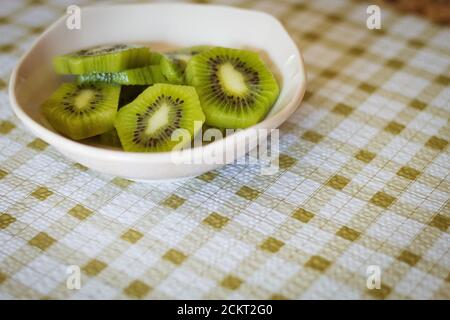Sliced kiwi in a pink bowl on checkered green tablecloth Stock Photo