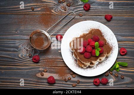 portion of Classic tiramisu dessert with raspberries on wooden background Stock Photo