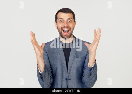 Young businessman with a smile man with a beard in a jacket, notes crazy and amazed with success with raised hands and open eyes shouting excitedly. Winner concept. Stock Photo