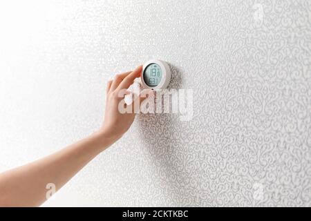 A woman's hand regulates the temperature on the thermostat in the house. The concept of a modern comfortable and technological home. Stock Photo