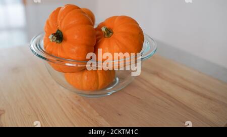 Glass bowl of miniature pumpkins on a wooden countertop. Background has space for copy. Stock Photo