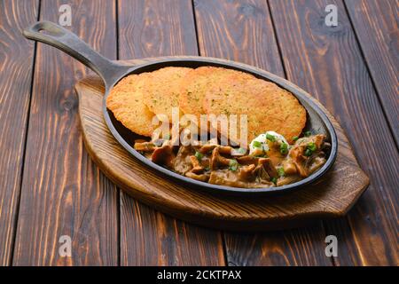 Cast iron skillet with fried chanterelles, honey mushrooms and potato pancakes with creamy sauce Stock Photo