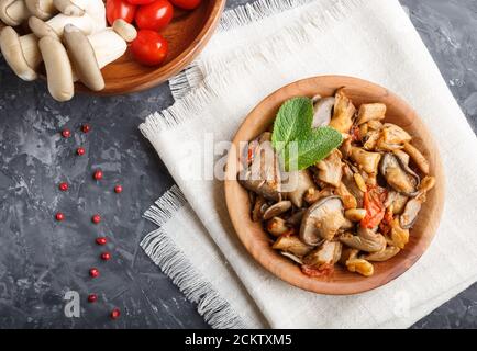 Fried oyster mushrooms with tomatoes in wooden plate on black concrete background. top view, close up. Stock Photo