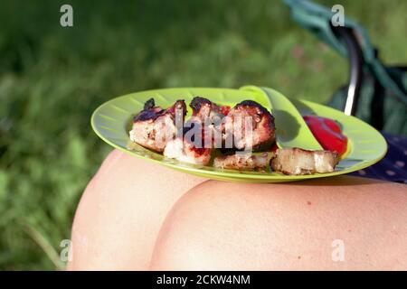 Grilled meat is on a plate. Plate on the lap of the girl. Close-up shot. Stock Photo