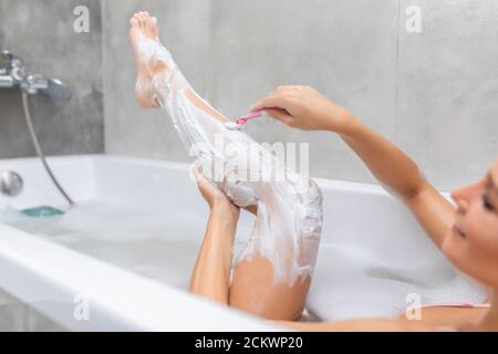 Woman shaving her leg with razor in bathroom. Stock Photo