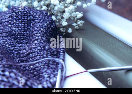 Craft and a bouquet of white flowers on a wooden bench. Texture beautiful knitted violet fabric with metallic fibers as background. Female hobby Stock Photo