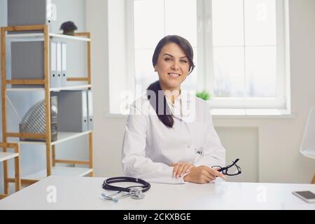 Female practicing doctor looking at the camera while sitting at a table in a clinic office. Stock Photo
