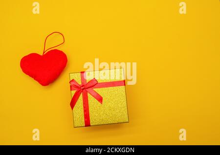Yellow shiny gift box, red heart on yellow background, top view, copy space. Greeting card for Valentine's day, holiday Stock Photo