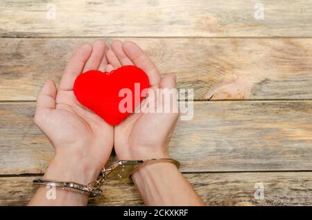 Man's handcuffed hands hold red heart on wooden background, copy space Stock Photo