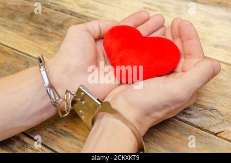 Man's handcuffed hands hold red heart on wooden background, copy space Stock Photo