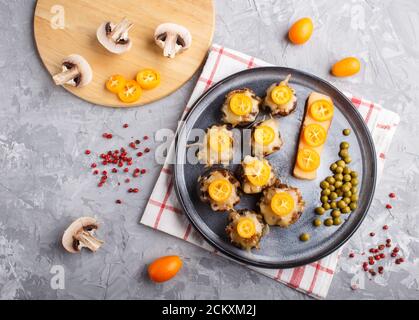 stuffed fried champignons with cheese, kumquats and green peas on a gray concrete background. ceramic plate, top view, flat lay, close up, horizontal. Stock Photo