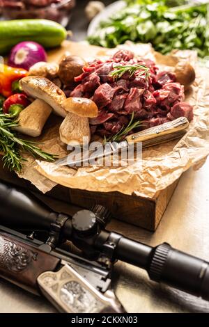 Sliced deer meat prepared for stew of game forest mushrooms herbs vegetables knife and hunter gun Stock Photo