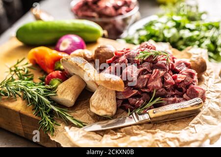 Sliced deer meat prepared for stew of game forest mushrooms herbs vegetables and knife Stock Photo