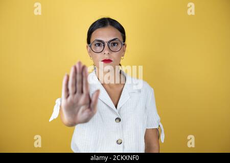 Beautiful woman over yellow background serious and doing stop sing with palm of the hand. Stock Photo