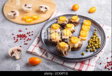 stuffed fried champignons with cheese, kumquats and green peas on a gray concrete background. ceramic plate, side view, close up, horizontal. Stock Photo