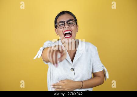 Beautiful woman over yellow background laughing at you, pointing finger to the camera with hand over body, shame expression. Stock Photo