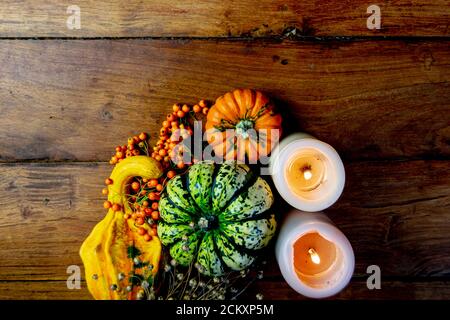 Flat lay composition made of pumpkins, rowan berries and candles on rustic wooden table and black background. Autumn symbolic vegetables in green Stock Photo