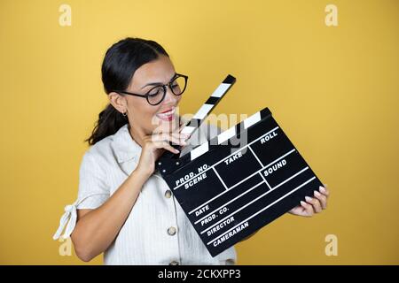 Beautiful woman over yellow background holding clapperboard very happy having fun Stock Photo