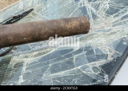 The iron pipe lies on the broken windshield of the car. Damage to the windshield with the power of an iron pipe, glass in cracks Stock Photo
