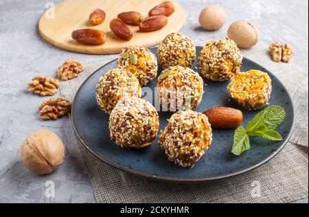 Energy ball cakes with dried apricots, sesame, linen, walnuts and dates with green mint leaves on a blue ceramic plate on a gray concrete  background. Stock Photo