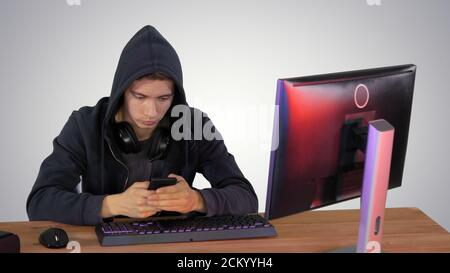 Hooded hacker using laptop and smartphone on gradient background Stock Photo