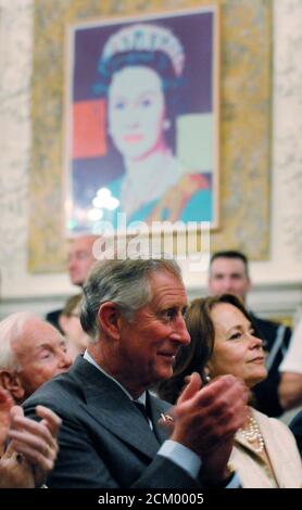 Britain's Prince Charles (C) applauds a musical performance as he sits beneath an Andy Warhol lithograph of his mother, Queen Elizabeth II, at a reception for the British Forces Foundation and United Service Organizations (USO) at the British Embassy in Washington, May 3, 2011. The Prince of Wales began a three-day visit to Washington on Tuesday to focus largely on environmental sustainability, the British Embassy said. REUTERS/Jonathan Ernst   (UNITED STATES - Tags: POLITICS MILITARY ROYALS)