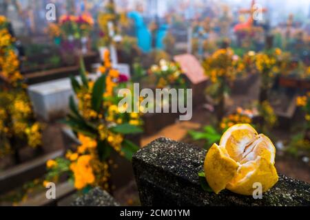 A fruit offering is seen placed on a stone cross amongst the decorated graves at a cemetery during the Day of the Dead celebrations in Ayutla, Mexico. Stock Photo