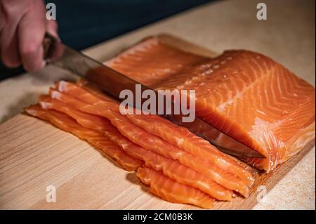 The woman chef slices or prepares fresh salmon fish fillets on the kitchen table. Stock Photo