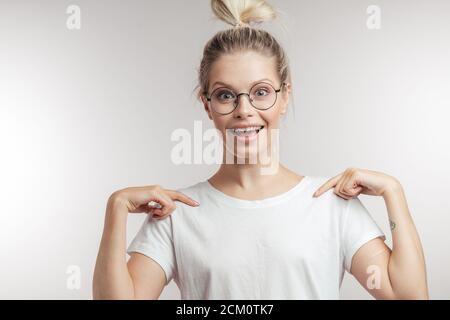 Shocked surprised beautiful blonde woman gets proposal from boyfriend, stares with bugged eyes, dressed in casual white t-shirt, isolated over white b Stock Photo