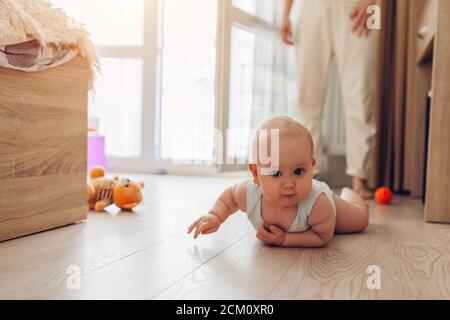 Infant crawling on floor in bedroom. Little baby having fun at home. Kid looks at camera Stock Photo
