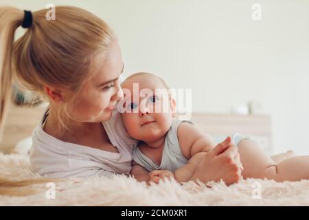 Woman lying on bed with her baby. Mother hugging kid. Family relaxing at home Stock Photo