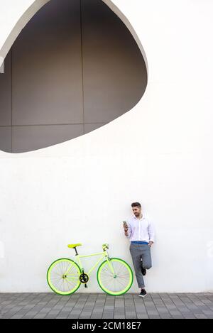 Young bearded man leaning against a white wall using the mobile phone Stock Photo