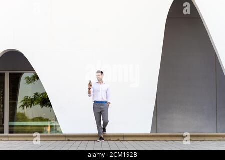 Young bearded man leaning against a white wall using the mobile phone Stock Photo