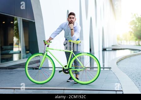 Young bearded man leaning on bicycle seat while looking at camera Stock Photo