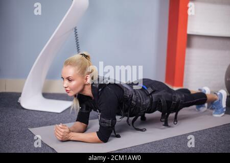 beautiful fit woman in ems fitness vest doing exercises in gym on mat in the sport center. wellnesss and health concept. side view full length photo Stock Photo