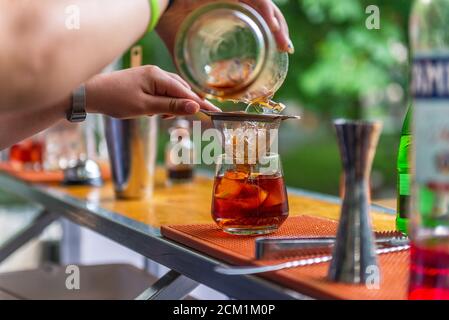 Cocktail close up. Bar or restaurant with blurred people in the background. Drink with single big ice cube. Stock Photo