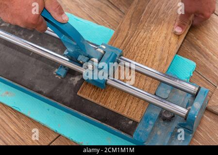 The man is cutting the floor tiles using a tile cutter machine. Stock Photo
