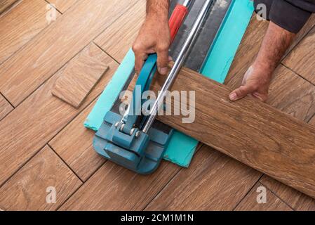 The man is cutting the floor tiles using a tile cutter machine. Stock Photo