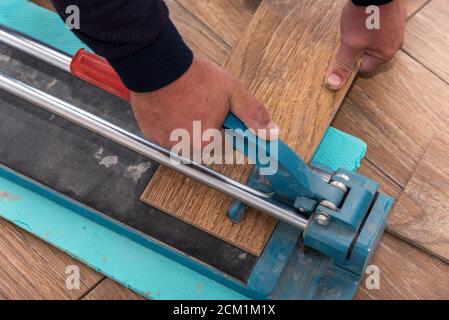 The man is cutting the floor tiles using a tile cutter machine. Stock Photo