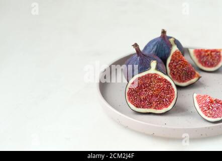 fresh ripe figs whole and cut into slices on stylish beige ceramic plate on gray empty background, selective focus Stock Photo